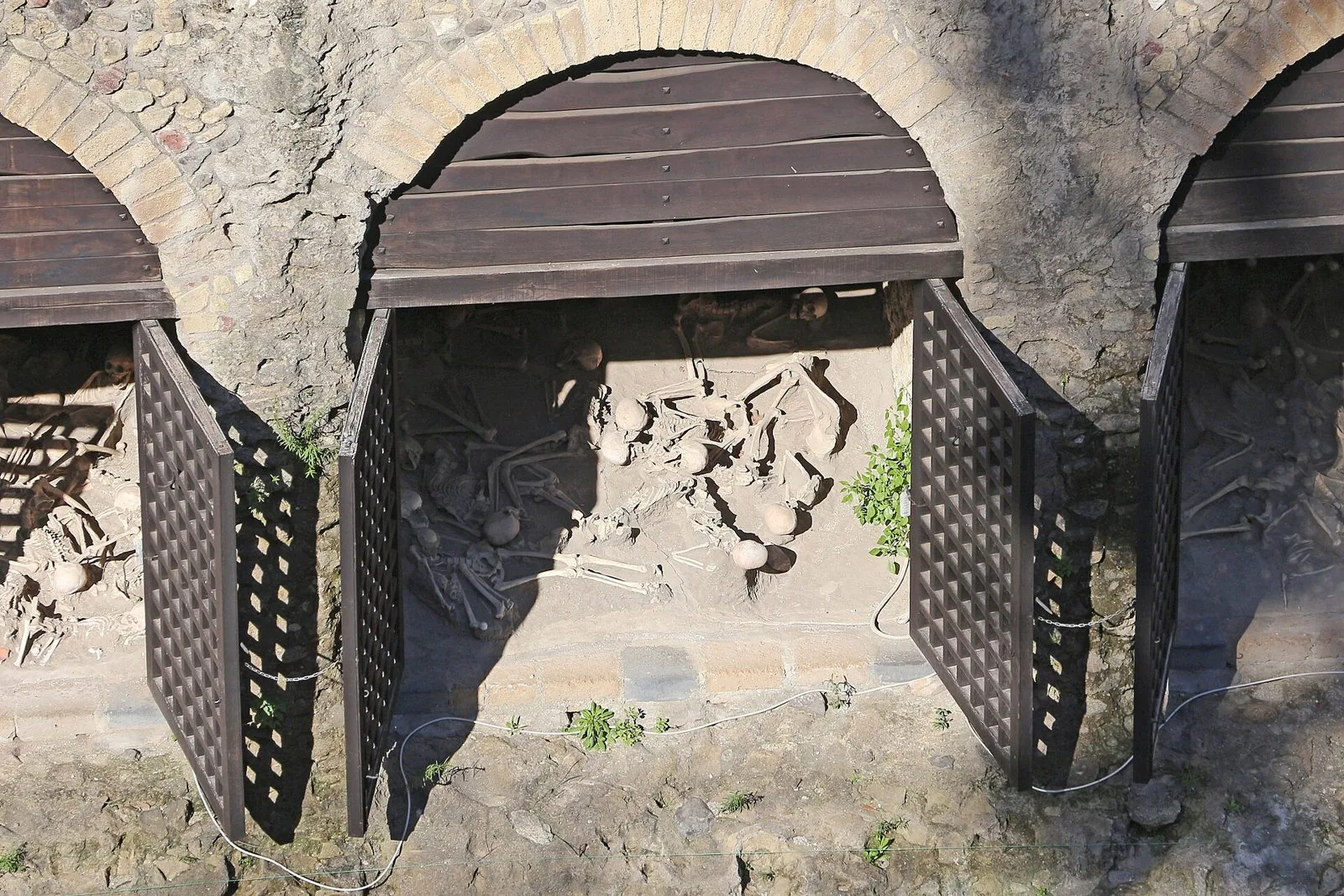 Fornici ad arco dell'antica spiaggia di Ercolano con resti scheletrici delle vittime dell'eruzione dietro grate di legno aperte