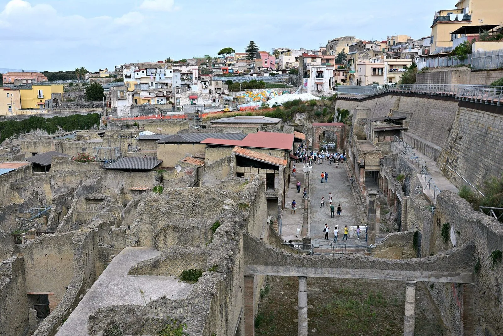Vista dall'alto degli scavi di Ercolano con le domus romane, il decumano massimo percorso dai visitatori e le case della città moderna sullo sfondo
