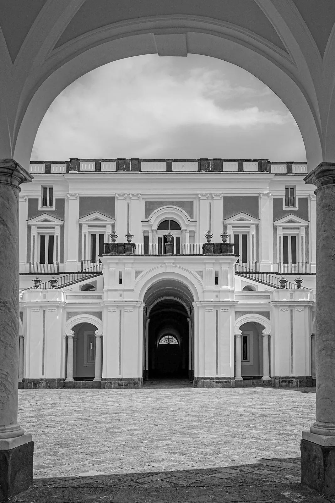 Facciata di Villa Campolieto a Ercolano vista attraverso un arco del portico, con lo scalone e il cortile lastricato, in bianco e nero