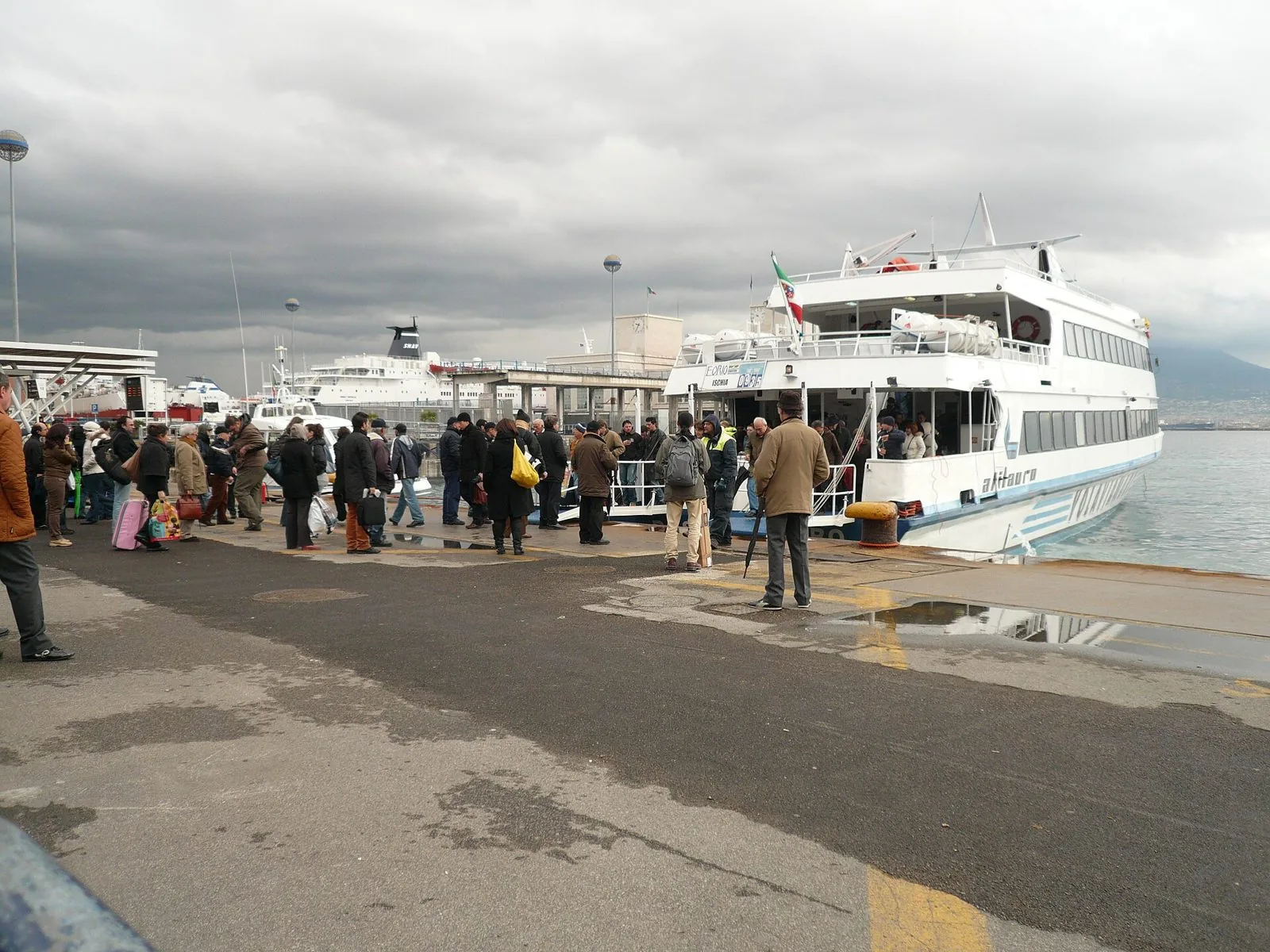 Passeggeri in attesa sulla banchina del Molo Beverello davanti a una motonave veloce attraccata nel porto di Napoli
