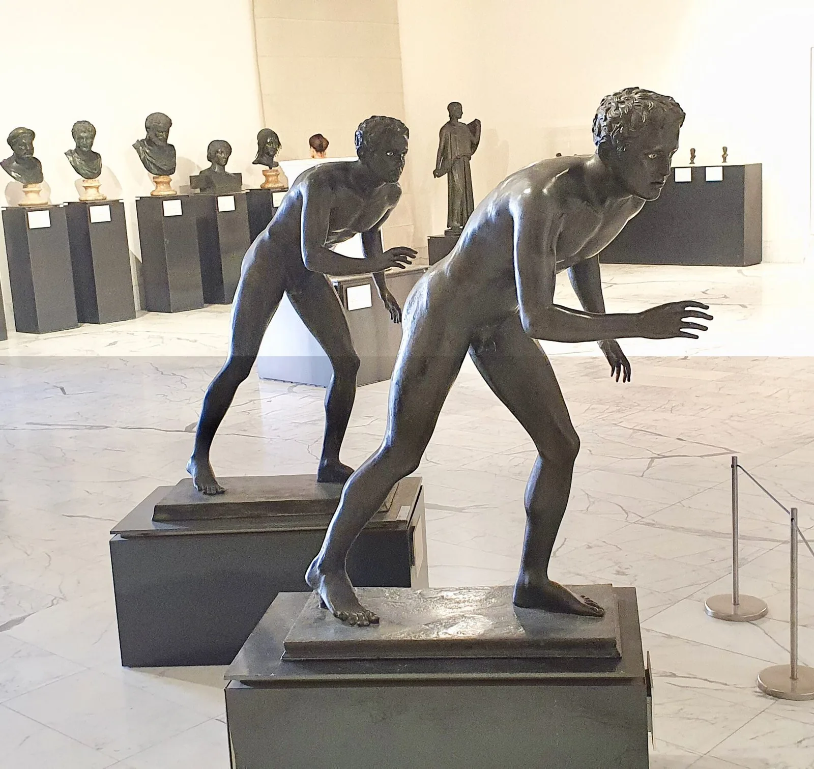 I due Corridori in bronzo dalla Villa dei Papiri esposti al Museo Archeologico Nazionale di Napoli, con busti bronzei sullo sfondo
